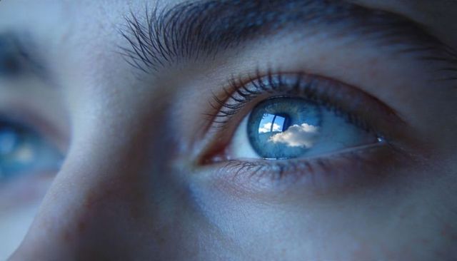 Macro close-up of blue eye reflecting window panes and cloud sky, youth gazing thoughtfully