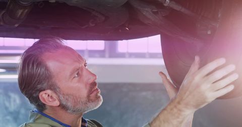 Mechanic inspecting tire underneath vehicle