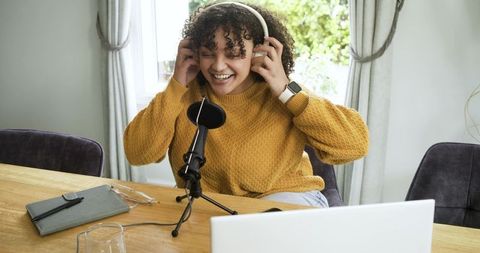 African american woman recording podcast at home with microphone and laptop, smiling