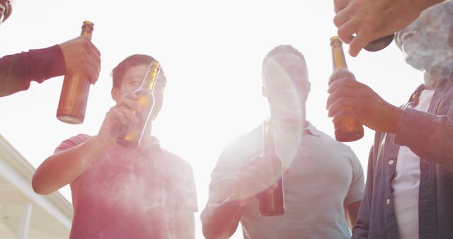 Men holding beer bottles and socializing outdoors under bright sunlight, creating a relaxed summer vibe. Ideal for use in promotions for social gatherings, party invitations, beverage advertising, and lifestyle content.