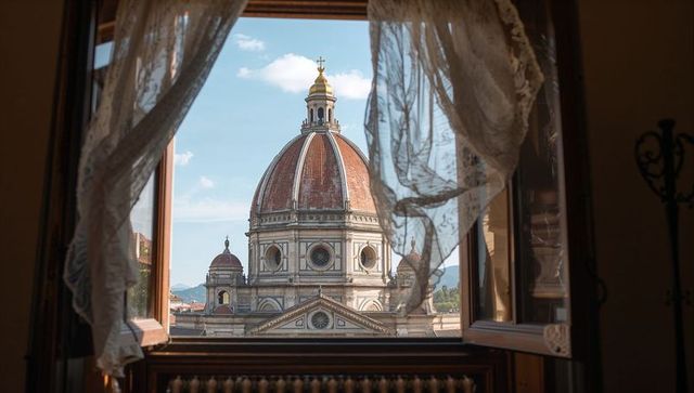 Open window framing historic cathedral dome with billowing lace curtains and radiator