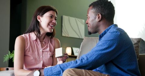 Interracial couple celebrating with gift exchanging on sofa
