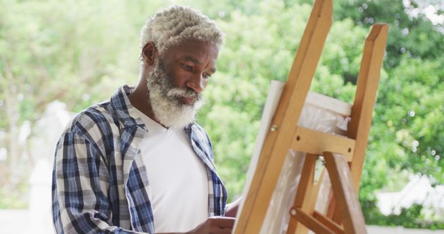 Image of african american senior man painting picture outside. retirement lifestyle, spending time alone at home concept digitally generated image.