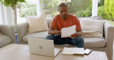 Man in Casual Attire Reviewing Papers While Seated on Sofa