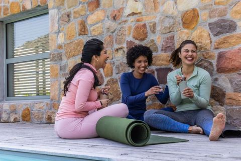 Three diverse women laughing and hydrating after outdoor yoga on pool deck