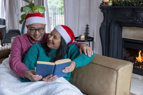Couple Sharing Book Wearing Santa Hats by Fireside
