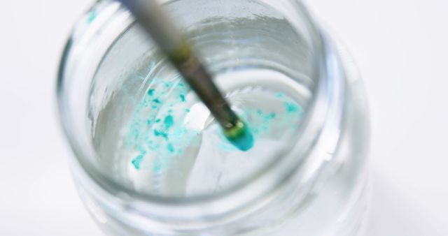 Close-up view of a cleaning brush in a jar with water, showing paint residue. Ideal for art education materials, artist blogs, and articles on cleaning art supplies.