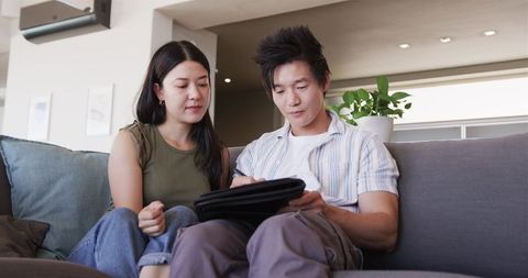 Young couple budgeting on tablet while sitting on sofa modern home financial planning