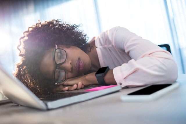 Businesswoman taking a nap on her desk in an office environment, showcasing fatigue and stress from work. Useful for illustrating concepts of workplace exhaustion, the importance of breaks, and the impact of overworking. Ideal for articles, blogs, and presentations on work-life balance, employee well-being, and productivity.