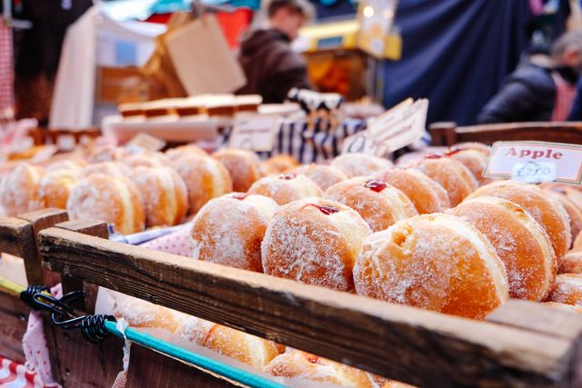 These doughnuts with various fruit fillings and sprinkled with sugar are arranged in wooden crates at a market stall. Ideal for use in food blogs, bakery advertisements, cooking magazines, or flyers promoting local markets and food festivals.