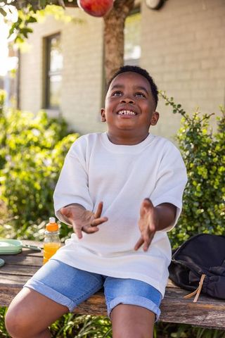 Joyful african american boy reaching for apple on garden bench outdoor summer lifestyle