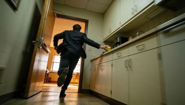 Executive running in office kitchen reaching for apple toward open door in rush