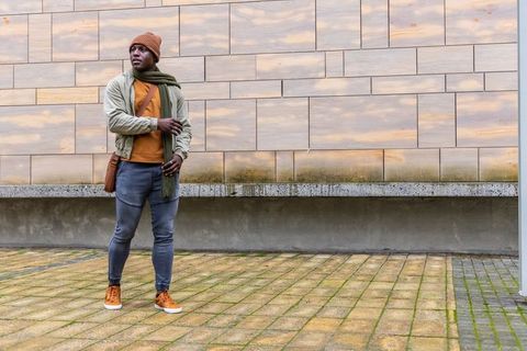 African american man standing in urban streetwear wearing scarf, beanie and crossbody bag