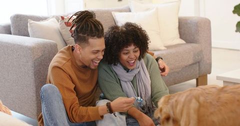 Couple playing with golden retriever on living room floor, cozy home moment