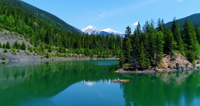 A serene lake surrounded by lush green forests with a majestic snow-capped mountain in the background, with copy space. A person enjoys a peaceful kayak trip, reflecting the beauty of nature and the tranquility of outdoor activities.