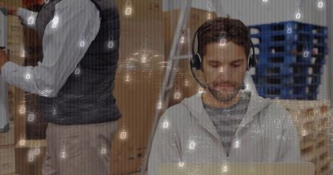 IT Specialist Typing in Warehouse Setting with Headset and Laptop