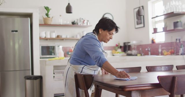 Senior biracial woman wearing apron and cleaning table in kitchen alone - Download Free Stock Photos Pikwizard.com