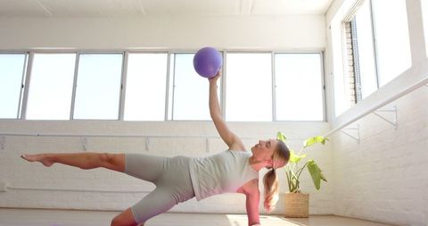 Caucasian Woman Practicing Yoga with Stability Ball in Bright Studio