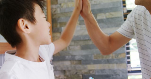 Father and son exchanging a high five, symbolizing a moment of joy and achievement. Perfect for illustrating family bonds, parental interaction, happiness, and supportive relationships in family-oriented content, educational materials, or advertisements.