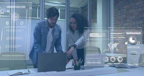Young professionals collaborating over laptop with holographic data overlays in modern office