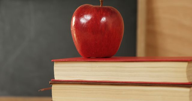 A red apple sits atop a stack of hardcover books, with copy space. Symbolic of education and learning, the apple is often associated with teachers and academic achievement.
