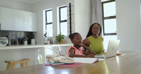 African American Mother Guiding Daughter Studying at Kitchen Table with Laptop Notebooks