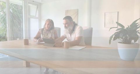 Senior couple reviewing documents and using tablet at sunlit dining table