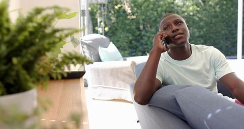 Man relaxing on sofa making phone call in bright minimalist living room with garden view
