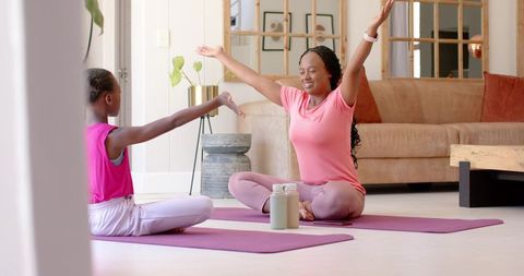 African American mother and daughter practicing seated yoga and stretching on purple mats