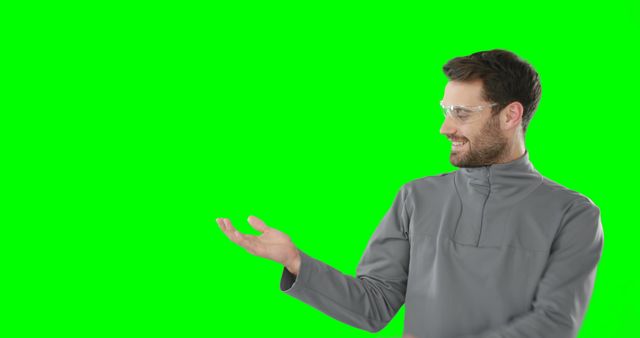 Man in casual grey sweater making presenting gesture against green screen background. Useful for business presentations, advertisements, and promotional content where custom content can be inserted on the green screen.