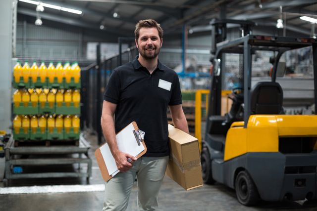 Portrait of smiling factory staff holding cardboard box and clipboard in factory