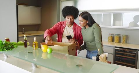 Couple Unpacking Groceries in Modern Kitchen Doing Online Checkout