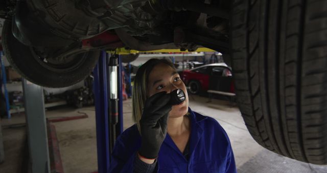 Female mechanic using a torch light and working under a car at a car service station. automobile repair service