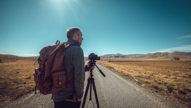 Photographer adjusting dslr on tripod while capturing remote mountain road landscape
