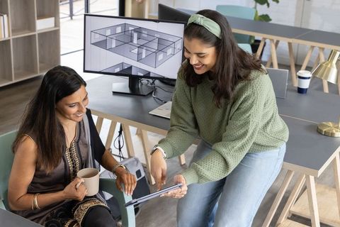 Diverse female team collaborating over tablet and floorplan in modern open-plan office