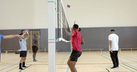 Men practicing indoor volleyball jumping and reaching at net during competitive training