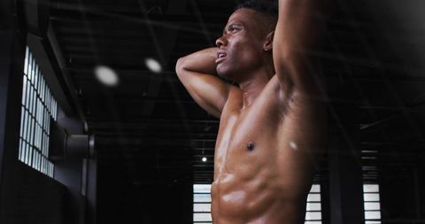 Muscular athlete training shirtless raising arms behind head in gritty industrial gym