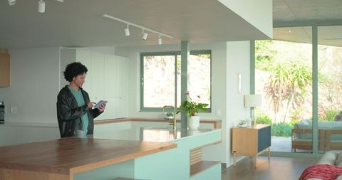 Mid-adult man using tablet at kitchen island in modern open-plan home interior