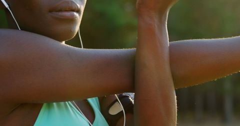 Athletic woman stretching arms with headphones in sunny forest setting