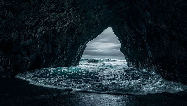 Triangular sea cave framing stormy teal ocean waves crashing into dark coastal cavern