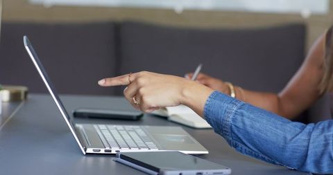 Diverse female coworkers pointing at laptop and taking notes during collaborative meeting