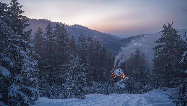 Glowing cabin nestled in snow-covered alpine forest at twilight with smoke rising