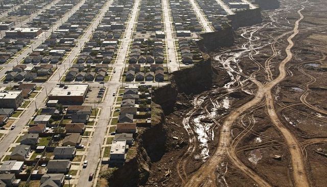 Aerial showing escarpment between suburb grid housing and cleared muddy land with tracks