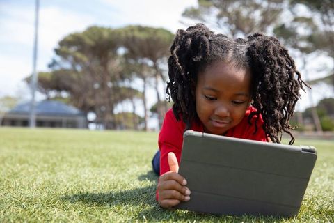 Young Girl Relaxing on Grass Using Tablet in Park