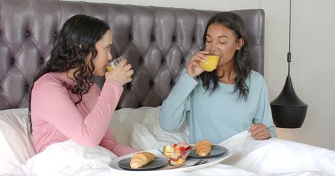 Diverse Female Friends Enjoying Breakfast in Bed with Fresh Orange Juice