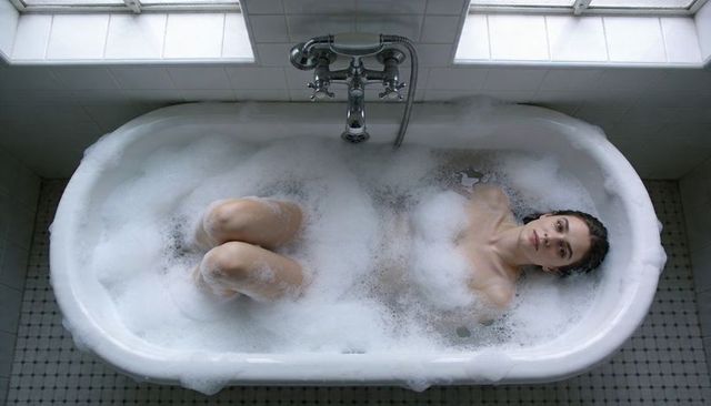 Overhead view woman relaxing in bubble bath in vintage clawfoot tub, soft natural light