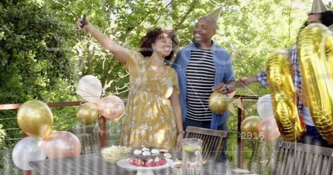Friends taking selfie on deck at backyard summer celebration with gold foil balloons and desserts
