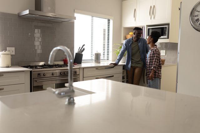 Smiling african american young man talking with girlfriend while standing by kitchen counter at home. unaltered, lifestyle, home, love and togetherness concept.