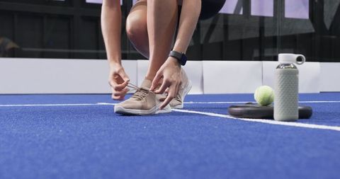 Athlete Tying Shoelaces on Padel Court with Equipment Nearby