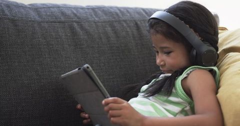 Young Girl Reclining on Sofa Enjoying Tablet Entertainment